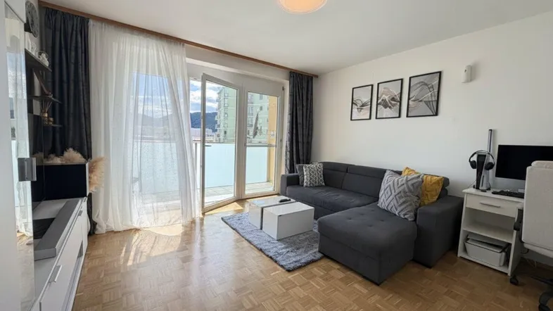 Helles Wohnzimmer mit modernem Sofa, Parkettboden und Zugang zum Balkon.