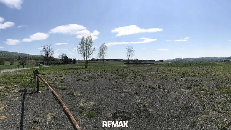 Panoramablick auf ein großes, unbebautes Grundstück mit Schotterfläche und grünen Feldern unter blauem Himmel.