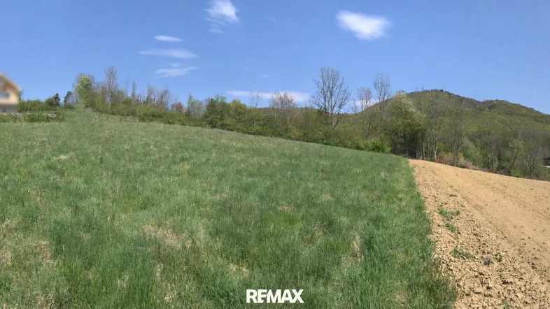 Panoramablick über grüne und beackerte Felder mit Hügeln und einem Haus im Hintergrund.