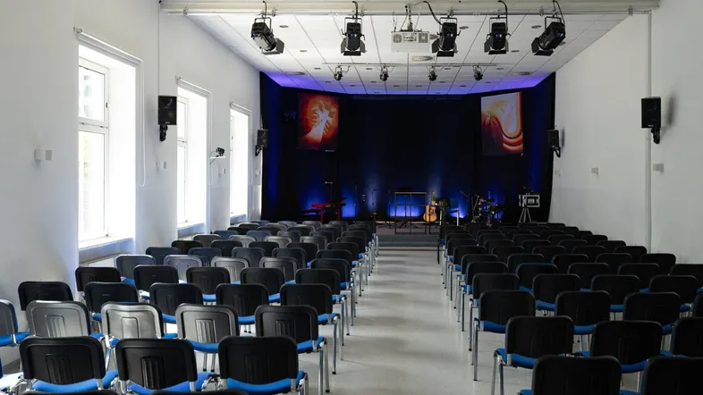 Großer Konferenzraum mit Reihen von Stühlen, einer Bühne und professioneller Beleuchtung für Veranstaltungen.