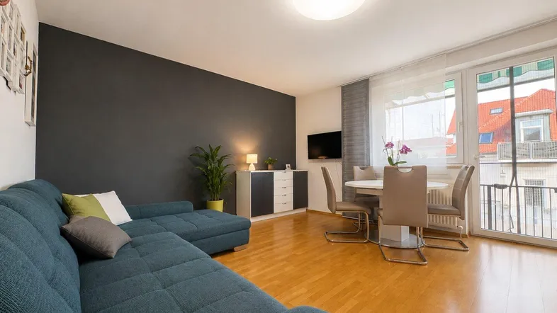Helles Wohn- und Esszimmer mit modernem Sofa, Esstisch und Zugang zum Balkon.