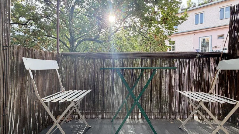 Sonnige Loggia mit Bambusabtrennung, zwei Stühlen und einem kleinen Tisch, ideal zum Entspannen.