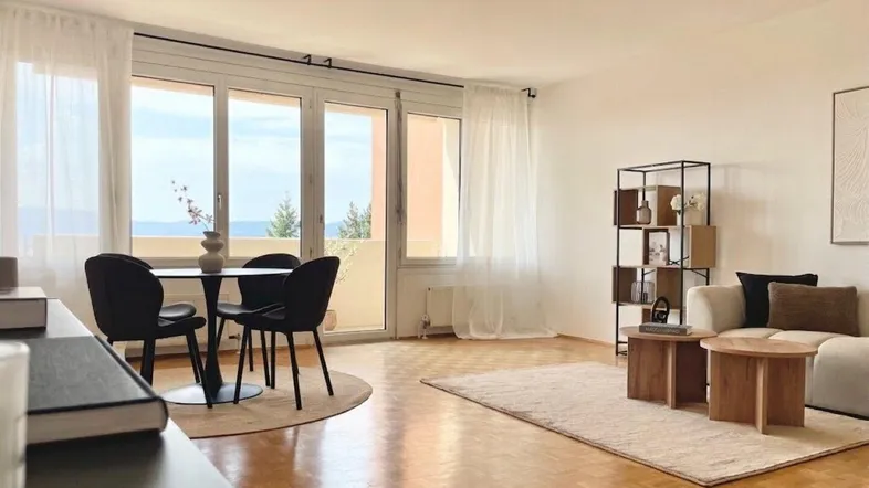 Helles Wohn- und Esszimmer mit Parkettboden, Balkonzugang und weitem Ausblick.