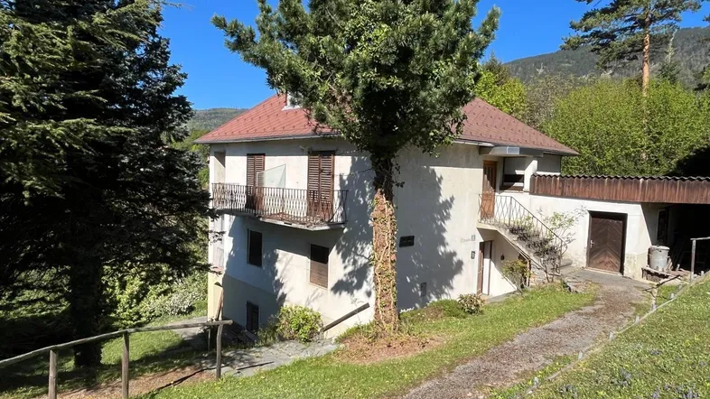 Traditionelles Haus mit Balkonen und umgeben von viel Grün in sonniger Lage.