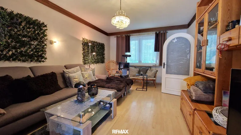 Gemütliches Wohnzimmer mit bequemer Couch, Holzbalken an der Decke und dekorativen Pflanzenwänden.