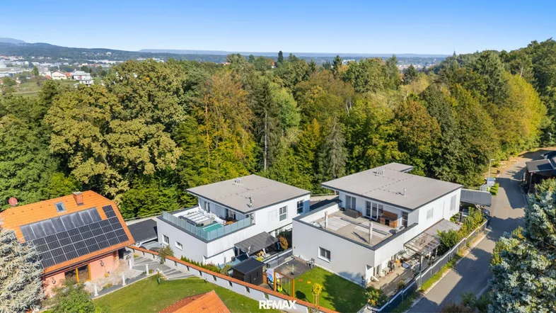 Luftaufnahme von modernen Häusern mit Flachdächern und Solaranlagen in grüner Umgebung.