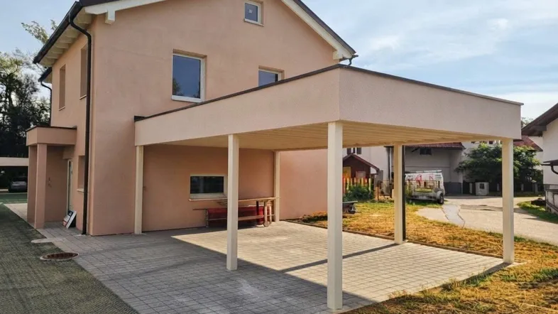 Modernes Einfamilienhaus mit Carport und gepflasterter Auffahrt unter blauem Himmel.