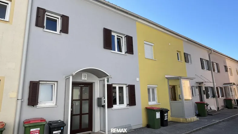 Reihenhäuser mit farbigen Fassaden und braunen Fensterläden unter blauem Himmel.