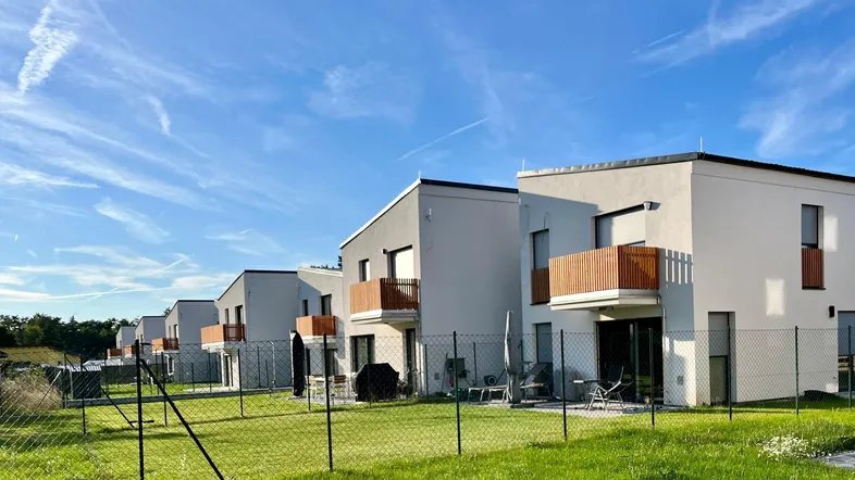 Reihen moderner Neubauten mit Flachdächern, Balkonen und kleinen Gärten unter blauem Himmel.