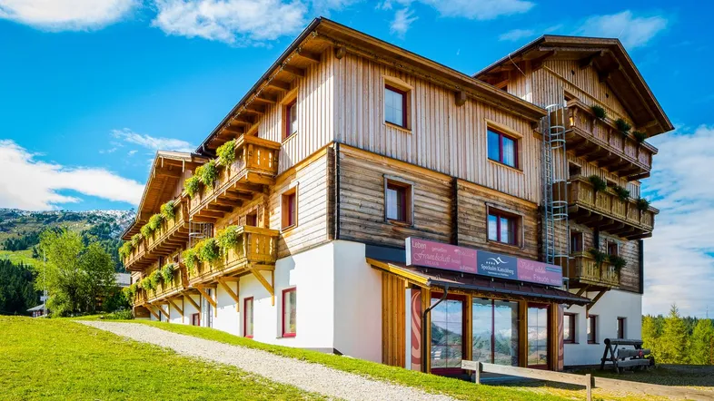 Holzverkleidetes Gebäude mit Balkonen und grüner Umgebung unter blauem Himmel.