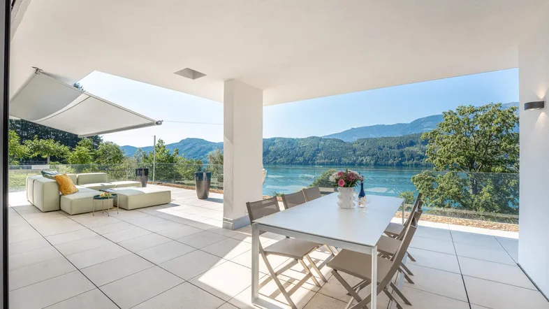 Geräumige Terrasse mit bequemen Loungemöbeln und Esstisch, bietet einen atemberaubenden Blick auf den See und die Berge.
