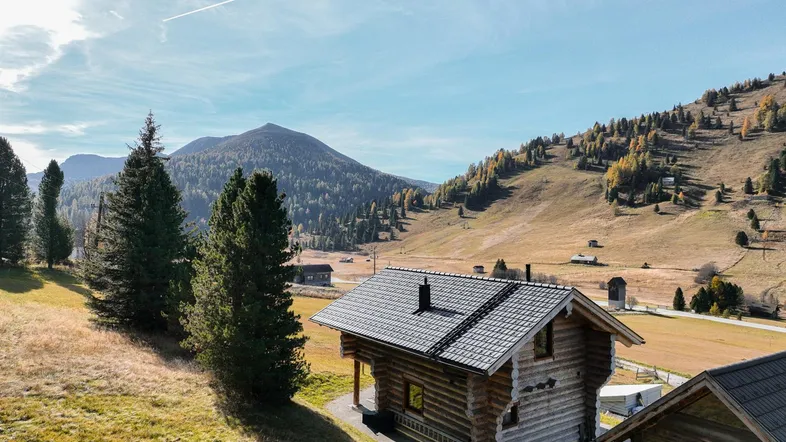 Rustikales Holzhaus in alpiner Berglandschaft unter blauem Himmel mit weiten Wiesen.