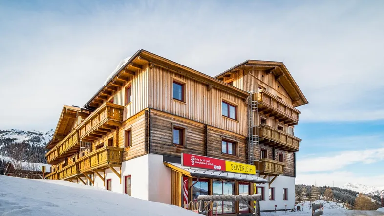 Traditionelles Holzgebäude im alpinen Stil, umgeben von Schnee und Bergen, mit Skiverleih im Erdgeschoss.