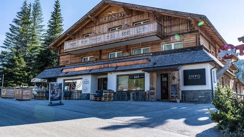 Traditionelles Holzgebäude mit Balkonen und einer einladenden Außenterrasse, umgeben von Bäumen.