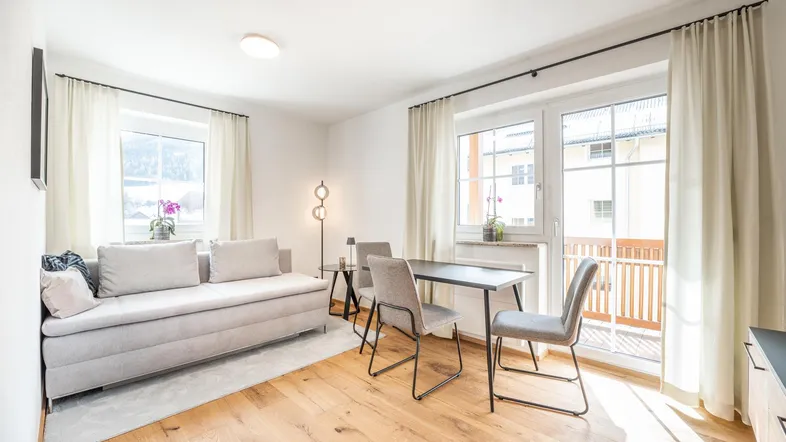 Helles Wohn- und Esszimmer mit Holzboden, bequemer Couch und Zugang zum Balkon.