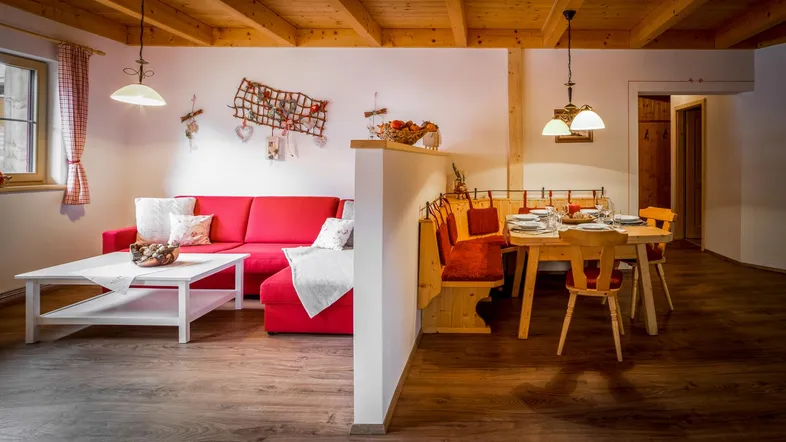 Helles Wohn- und Esszimmer im alpinen Stil mit Holzbalkendecke und gemütlichem roten Sofa.
