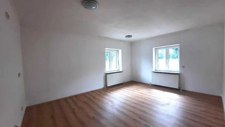 Heller, leerer Raum mit Laminatboden und zwei Fenstern, bereit für eine Renovierung.