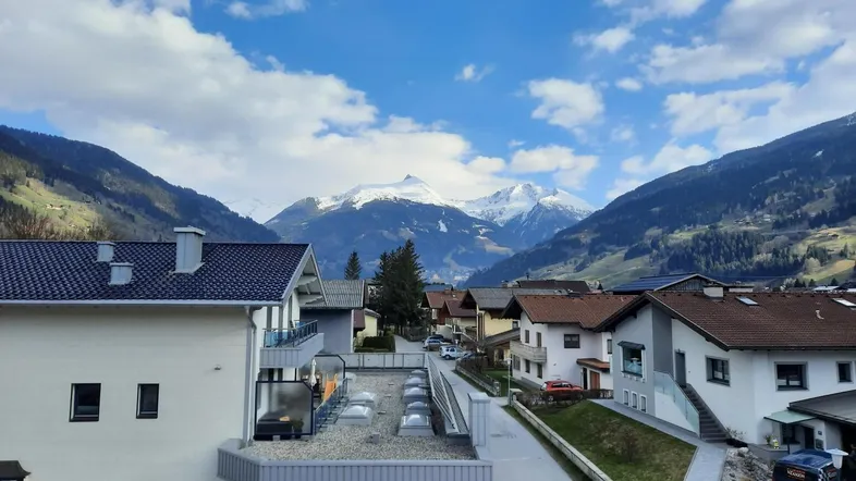 Panoramablick über ein alpines Dorf mit traditionellen Häusern und majestätischen schneebedeckten Bergen im Hintergrund.