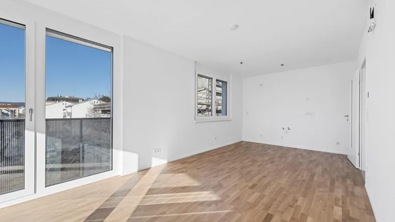 Helles, leeres Zimmer mit Parkettboden und Zugang zu einem Balkon, ideal für Wohn- oder Schlafbereich.