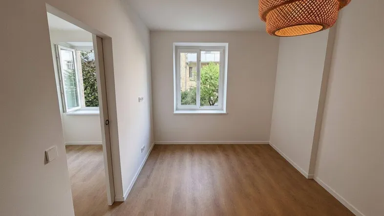 Helles Zimmer mit Holzboden, weißen Wänden und einem Fenster, das den Blick nach draußen freigibt.