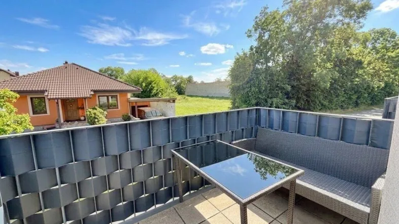 Heller Balkon mit Sitzgelegenheiten und Blick auf die grüne Umgebung und ein Einfamilienhaus.