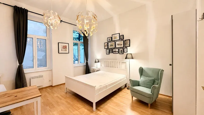 Helles Schlafzimmer mit Holzboden, einem bequemen Sessel und dekorativen Wandbildern.