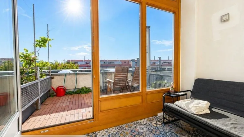 Heller Innenraum mit großen Holzfenstern, die auf die sonnige Dachterrasse blicken.