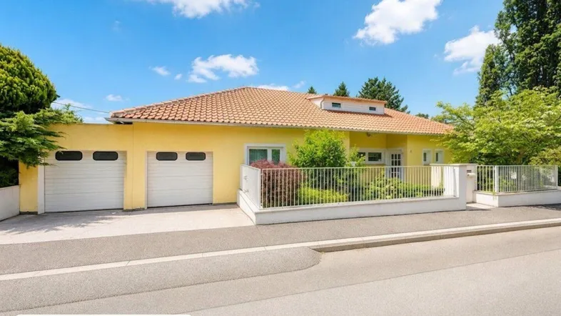 Gelbes Einfamilienhaus mit rotem Ziegeldach, zwei Garagen und gepflegtem Vorgarten.