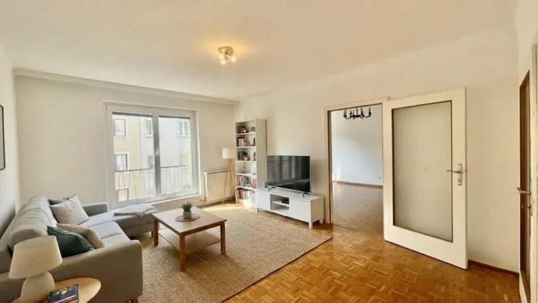 Helles Wohnzimmer mit Parkettboden, gemütlichem Sofa und Zugang zu einem Balkon.