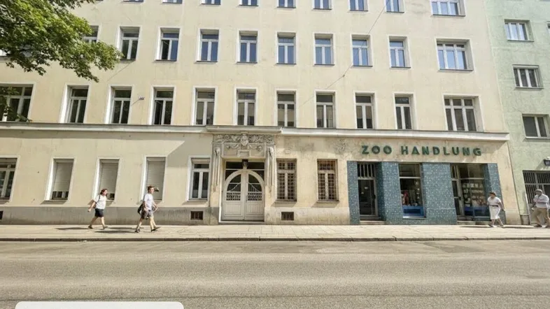 Gebäudefassade eines Mehrfamilienhauses mit Geschäften im Erdgeschoss und klassischer Architektur an einer Stadtstraße.