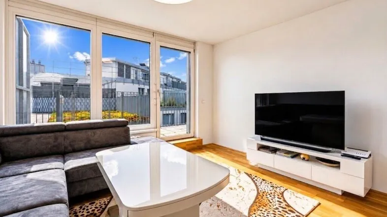 Helles Wohnzimmer mit großem Sofa, modernem Couchtisch und Zugang zu einer sonnigen Terrasse.