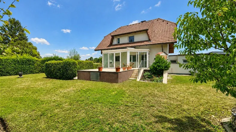 Großzügiger Gartenbereich mit gepflegtem Rasen, Hecken und einem Wintergarten am Haus.