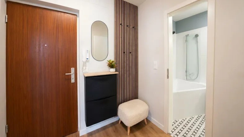Moderner Eingangsbereich mit Holztür, Schuhschrank und Blick in ein Badezimmer mit Dusche und Badewanne.