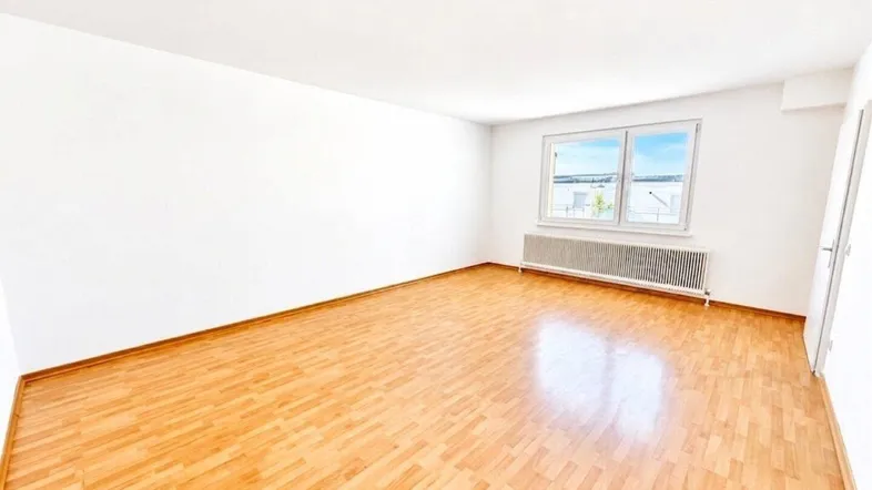 Geräumiges, helles Zimmer mit Parkettboden und einem Fenster, das viel Tageslicht hereinlässt.