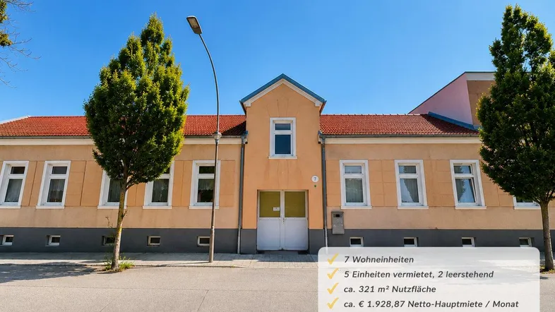Gelbe Fassade eines Mehrfamilienhauses mit mehreren Fenstern und einem Eingangsbereich unter blauem Himmel.