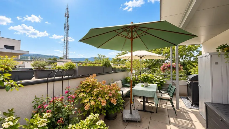 Große, sonnige Dachterrasse mit Gartenmöbeln, vielen Pflanzen und weitem Blick über die Stadt.