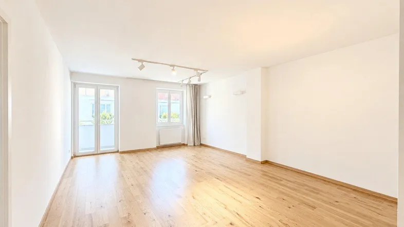 Helles, leeres Wohnzimmer mit Holzboden und Zugang zu einem französischen Balkon.