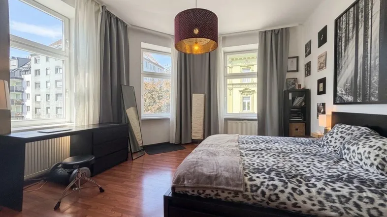 Helles Schlafzimmer mit Holzboden, großen Fenstern und moderner Hängelampe.
