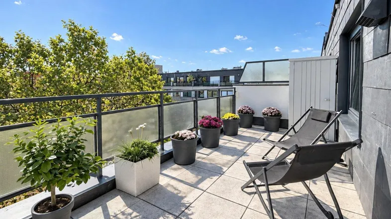 Sonnige Dachterrasse mit bequemen Liegestühlen, Pflanzen und weitem Blick über die Stadt.