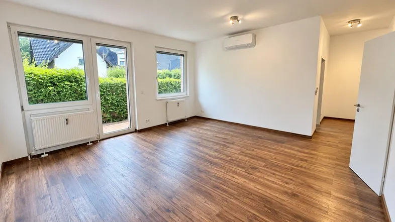 Helles Wohnzimmer mit Laminatboden, Klimaanlage und Zugang zu einem kleinen Außenbereich.