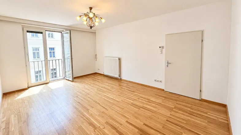 Helles Zimmer mit Holzboden, weiß gestrichenen Wänden und Zugang zu einem französischen Balkon.