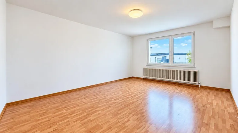 Heller, leerer Raum mit Laminatboden und großem Fenster, ideal als Wohn- oder Schlafzimmer.