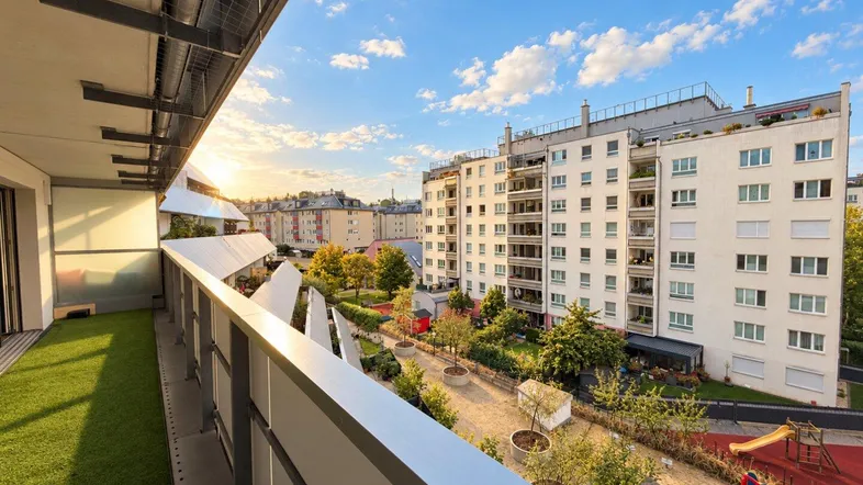 Geräumiger Balkon mit Kunstrasen und Blick auf die umliegenden Gebäude und einen Spielplatz.