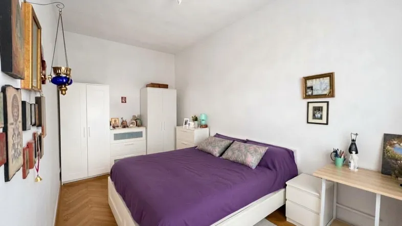 Helles Schlafzimmer mit lila Bett, weißen Kleiderschränken und Fischgrätparkettboden.