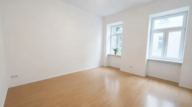 Heller, leerer Raum mit hellem Holzboden und zwei Fenstern, bereit zur individuellen Gestaltung.