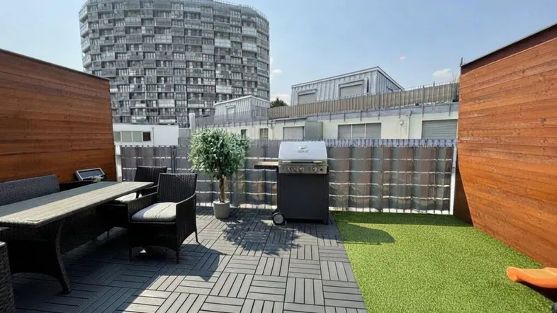 Geräumige Dachterrasse mit Essbereich, Grill und Blick auf moderne Stadtarchitektur.