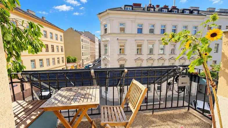 Sonniger Balkon mit Holztisch und Stühlen, bietet einen Blick auf die umliegenden Stadtgebäude.