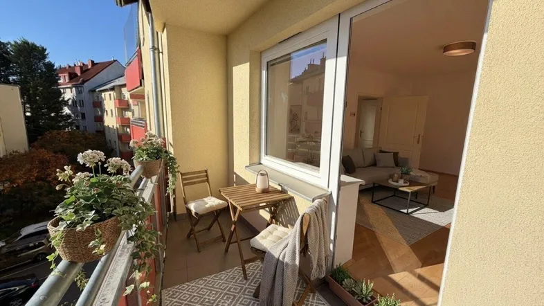 Gemütlicher Balkon mit Sitzgelegenheiten, Pflanzen und Blick auf die umliegenden Gebäude.
