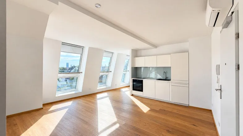 Helles Wohnzimmer mit integrierter Küchenzeile, Holzboden und großen Dachfenstern.