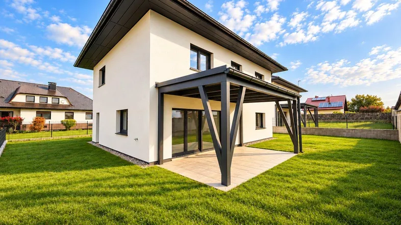 Modernes Einfamilienhaus mit weißer Fassade, dunklem Dach und überdachter Terrasse im Grünen.